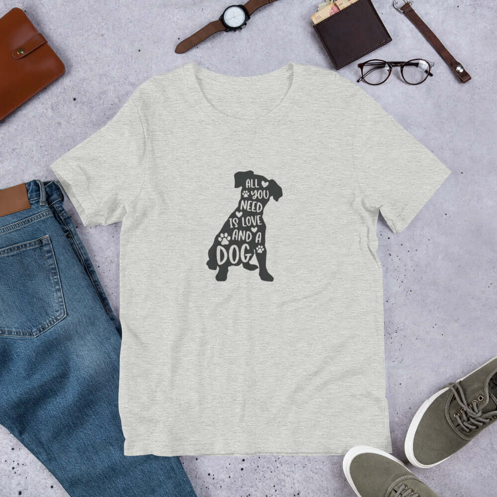 Gray t-shirt with a dog graphic and text on a gray surface with jeans, shoes, and accessories.